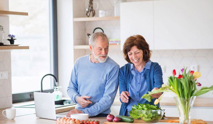 Um Retrato de casal senior com o laptop em casa cozinhando feliz