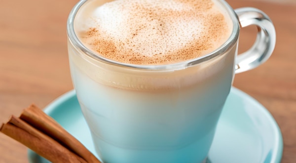 Foto da receita de Café Gelado Proteico. Observa-se uma xícara de vidro com a bebida dentro, polvilhada de canela. Foto gerada por IA.