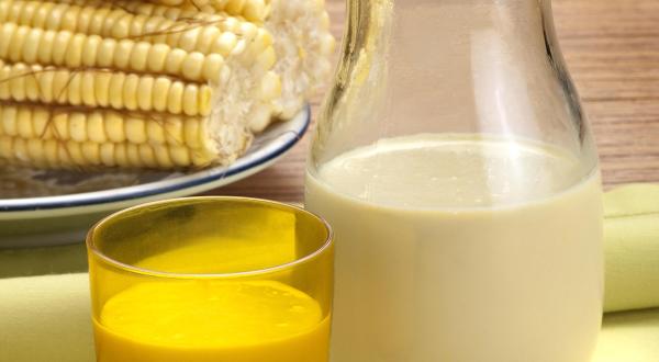 foto tirada de uma jarra com suco de milho e à frente um copo amarelo com a bebida