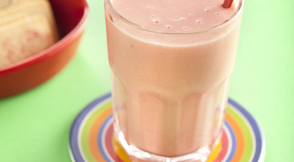 fotografia em tons de verde e rosa tirada de um copo transparente com a vitamina de frutas, e por cima um coração para decorar